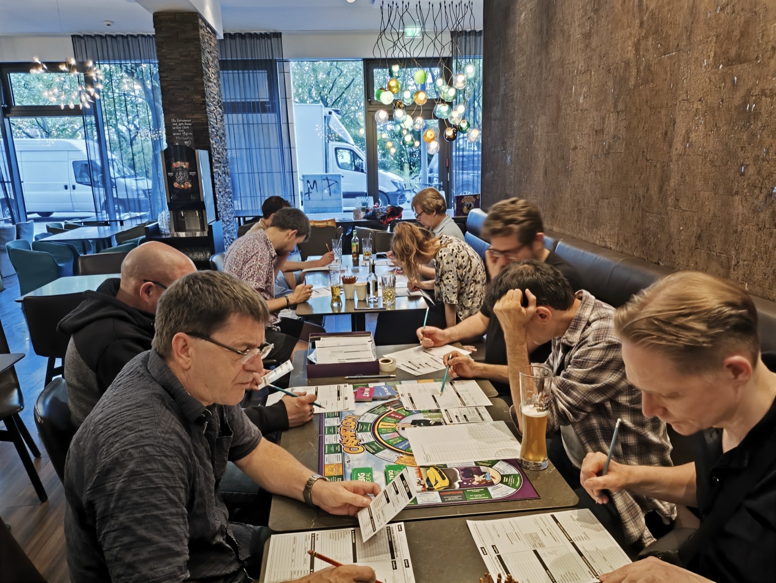Teilnehmende füllen ihre Spielbögen aus, Spielbrett auf dem Tisch